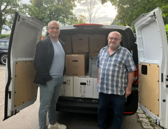 Auf dem Foto sind zwei Männer, die vor einem Transporter mit Umzugskartons stehen.