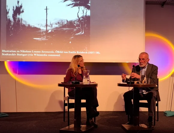 Das Foto zeigt Dr. Olivia Spiridon und Georg Aescht. Sie sitzen an kleinen Tischchen und disktieren.