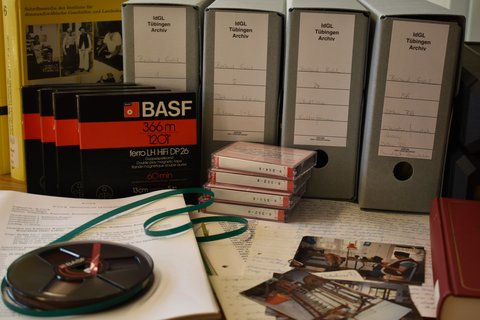 Die Abbildung zeigt, wie der Nachlass von Hans Gehl aufgearbeitet wird. Abgebildet sind Tonträger, Fotografien und schriftliches Material.