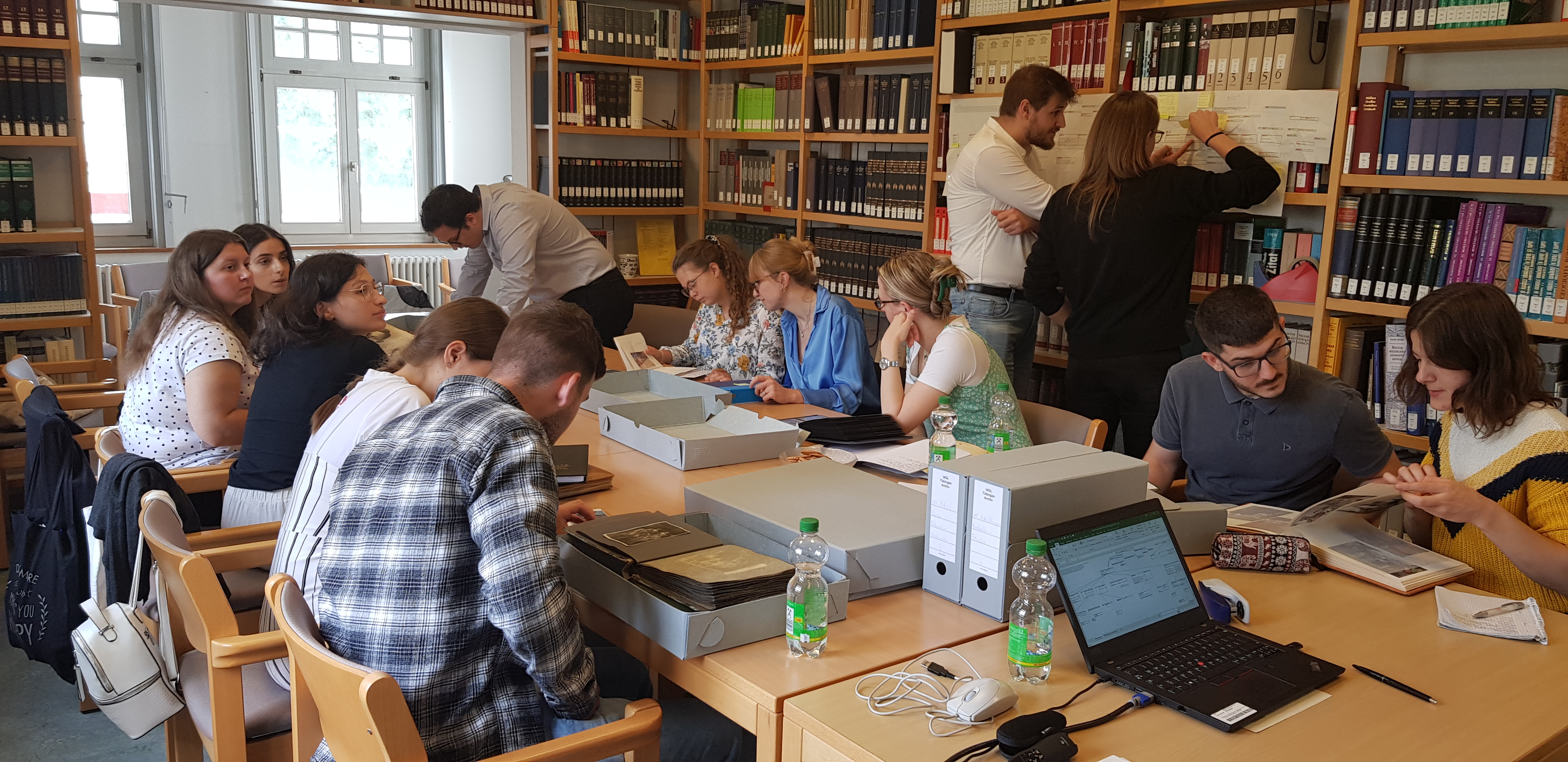 Studierende arbeiten mit Dokumenten an einem großen Tisch im Institut