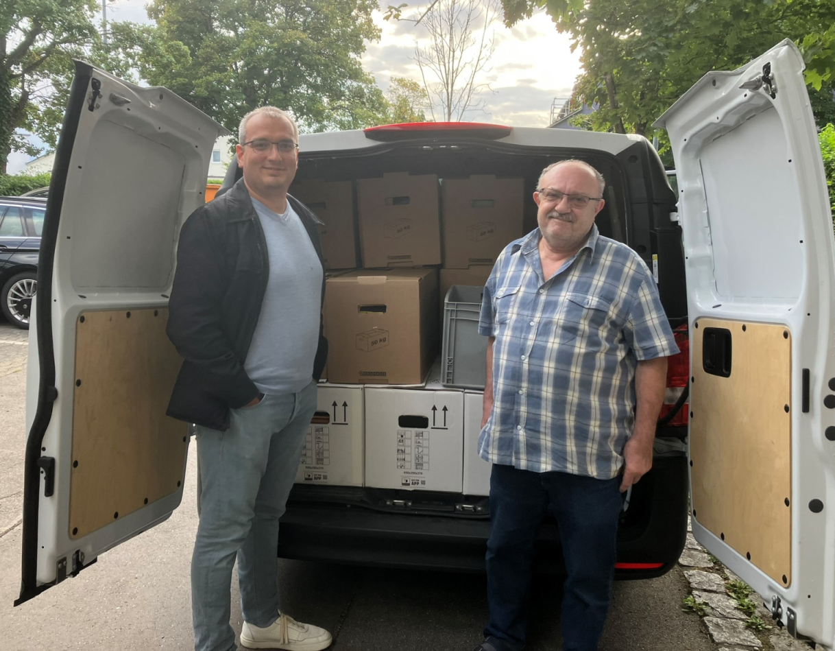 Auf dem Foto sind zwei Männer, die vor einem Transporter mit Umzugskartons stehen.