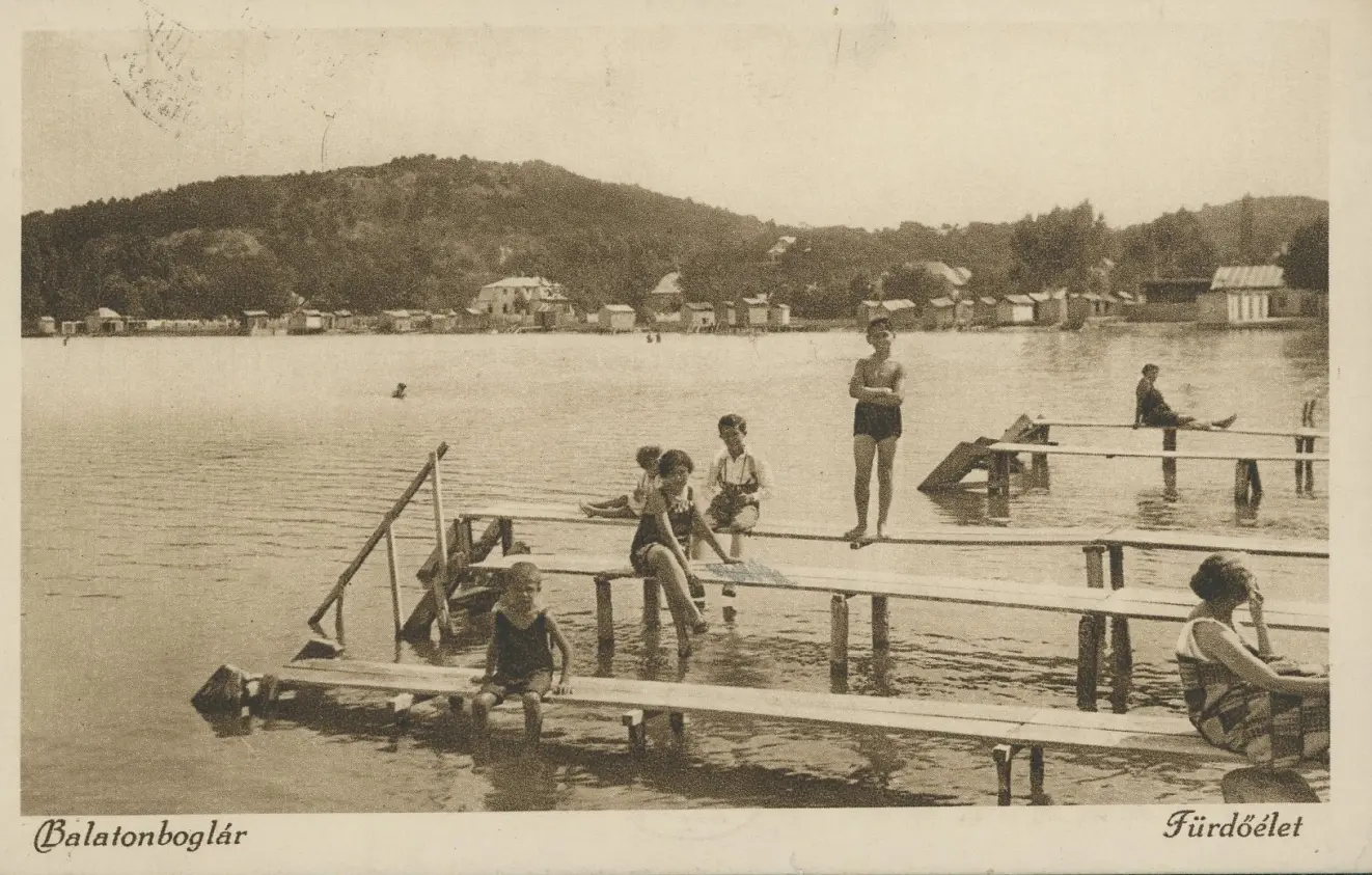 Das Bild zeigt eine historische Postkarte des Plattensees mit Personen, die in Badekleidung auf Stegen sitzen oder stehen.