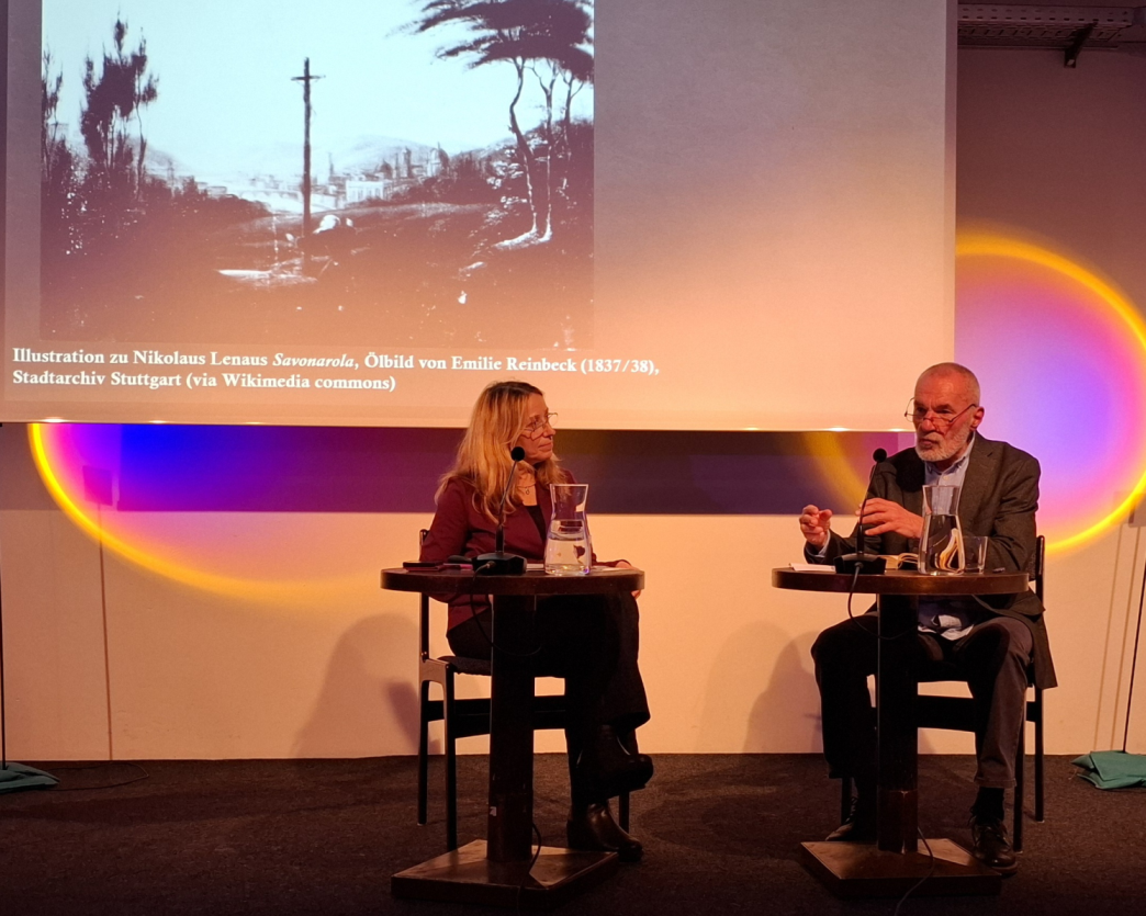 Das Foto zeigt Dr. Olivia Spiridon und Georg Aescht. Sie sitzen an kleinen Tischchen und disktieren.