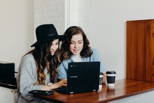 Das Bild zeigt 2 junge Frauen, die in einen Computer schauen.