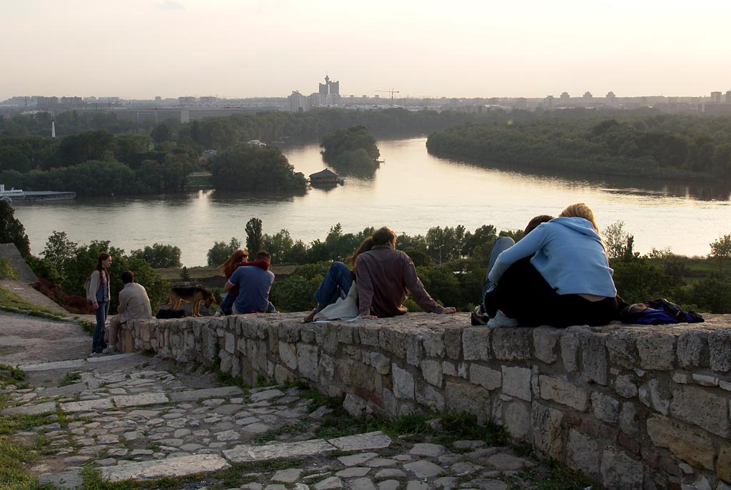 Das Bild zeigt Menschen, die auf einer Mauer oberhalb der Donau sitzen.