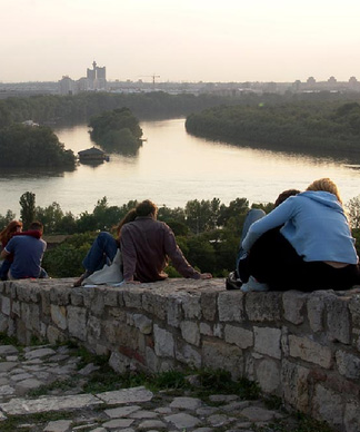 Menschen sitzen auf einer Mauer oberhalb der Donau